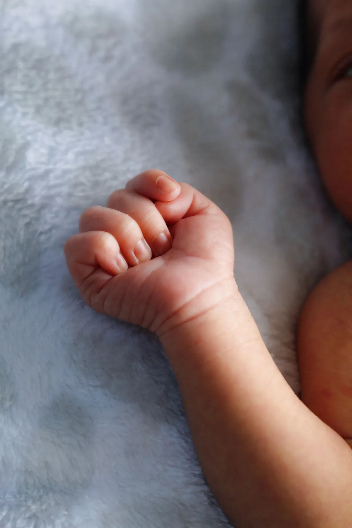Een pasgeboren baby met een gebalde vuist op een zacht dekentje