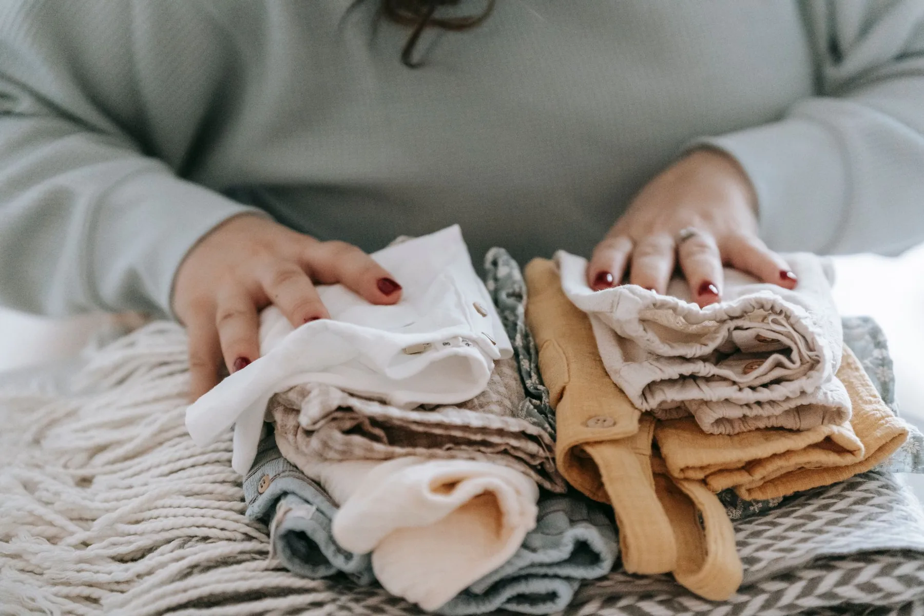 Handen vouwen kleine babykleertjes op een gebreide deken